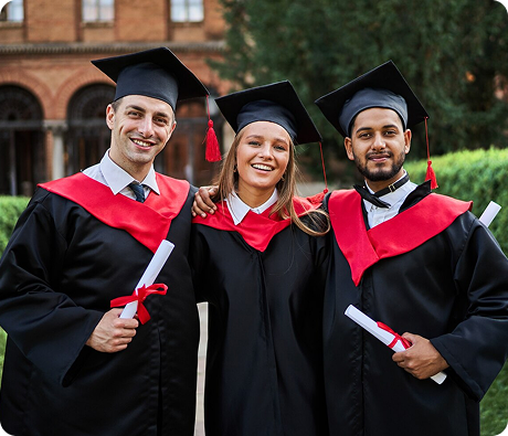 Three graduates wearing caps and gowns holding their diplomas outdoors.